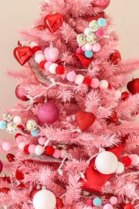 closeup of pink Christmas tree with red, white, and pink pom garland and red heart ornaments, pink glitter ornaments and white ornaments