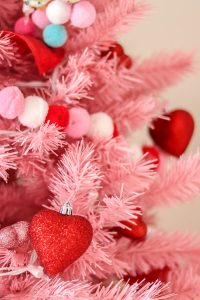 closeup of pink Christmas tree with red, white, and pink pom garland and red heart ornaments