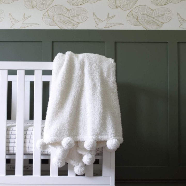 dark green board and batten wall with wallpaper and white crib
