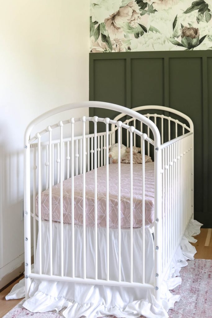 white metal crib against a dark green feature wall in nursery
