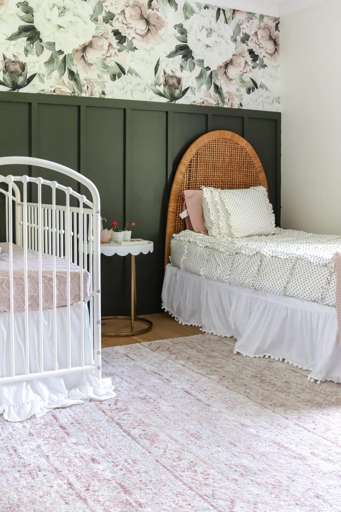 shared girls room with floral and hunter green feature wall with white metal crib and vintage woven headboard