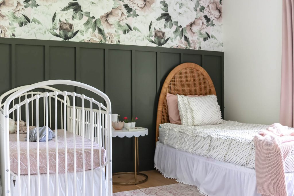 shared girls room with floral and hunter green feature wall with white metal crib and vintage woven headboard