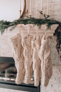 minimalist christmas decor ideas with white knit stockings on mantle with green garland