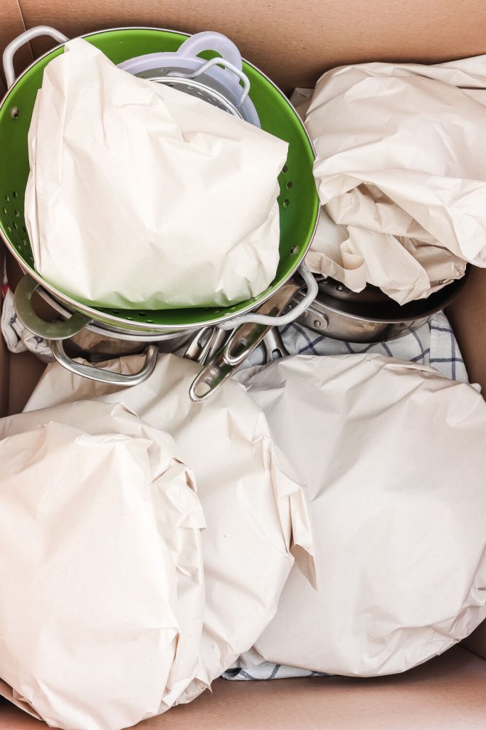 how to pack pots and pans with lids wrapped in packing paper and green collander