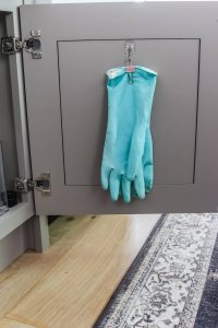 greige kitchen cabinet door open with teal cleaning gloves hanging on the door