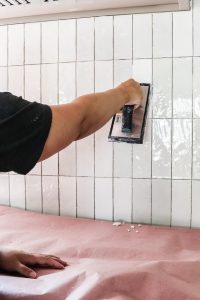 woman with black short sleeve shirt showing how to grout kitchen tile with grout float