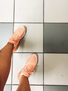 woman wearing peach nike shoes standing on bathroom floor with big square tiles