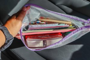 woman's hand holding open zipper bag with stuff in it for traveling with kids