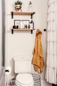 kids brown hooded towel hanging on hook with toilet and over the toilet shelves with white ruffle shower curtain