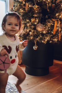 little girl in reindeer romper holding out ornament