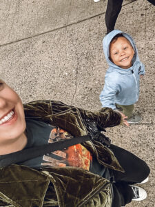 woman holding hand of little boy in gray jacket with hood on
