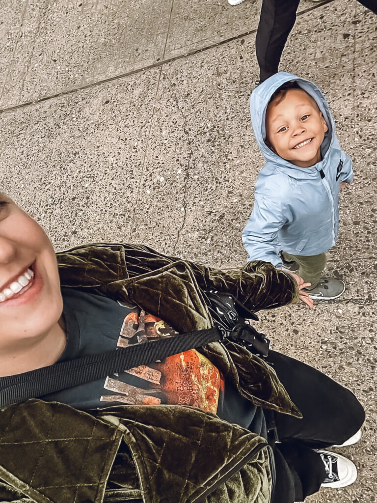 woman holding hand of little boy in gray jacket with hood on