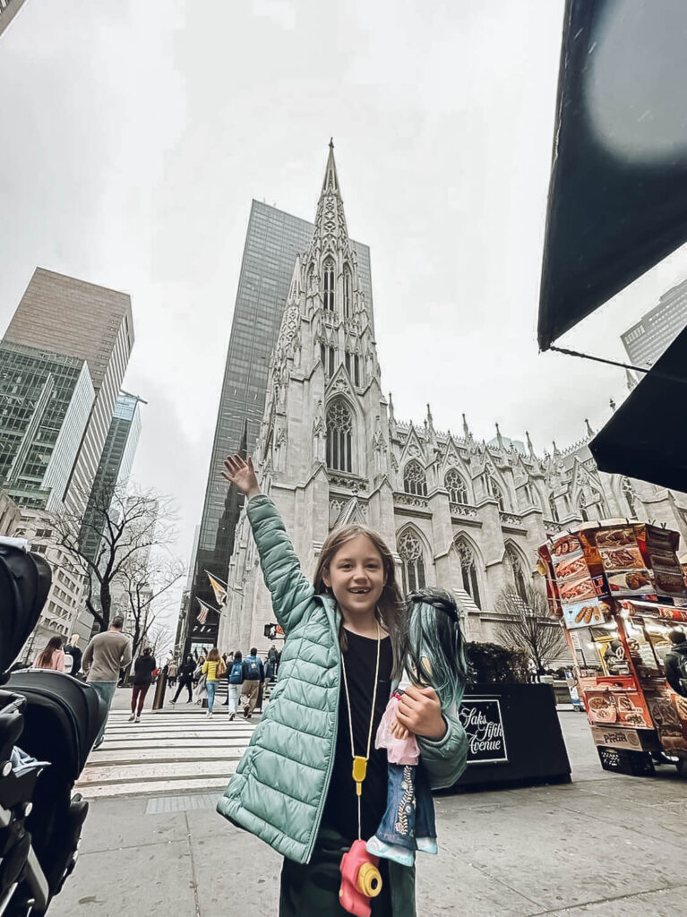 little girl in teal jacket standing in front of large building in New York City