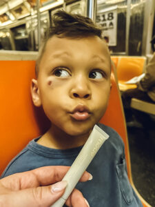 little boy on subway making kiss lips with lip gloss in front of his face