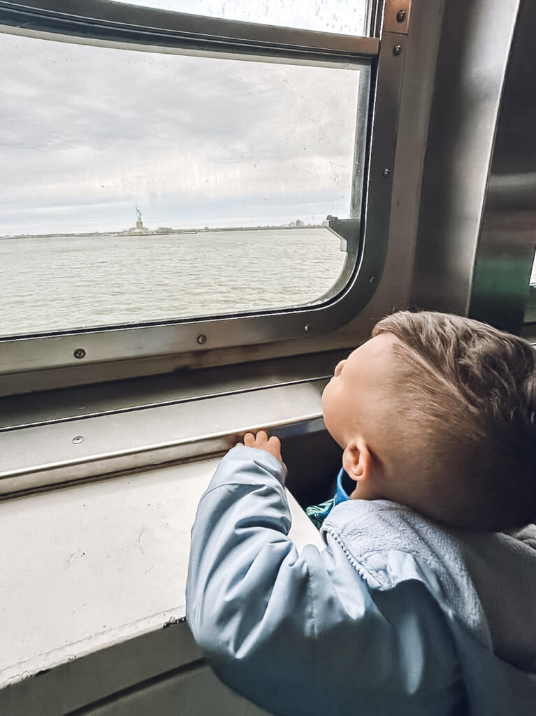 little boy looking out the window on the Staten Island Ferry looking at the Statue of Liberty