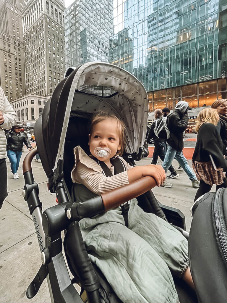 little girl in green jumper in overalls in stroller in New York City