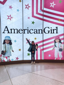 little girl in front of American Girl sign in New York City