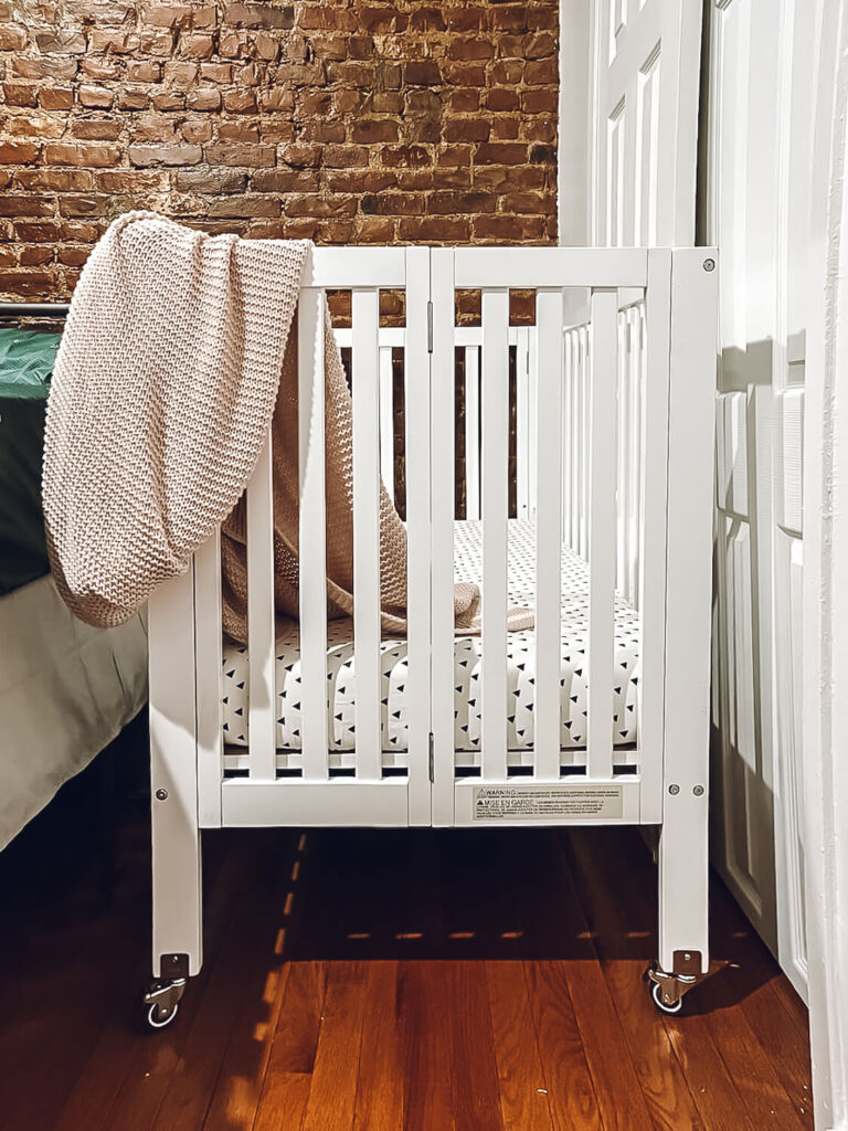 white portable crib in front of exposed brick wall