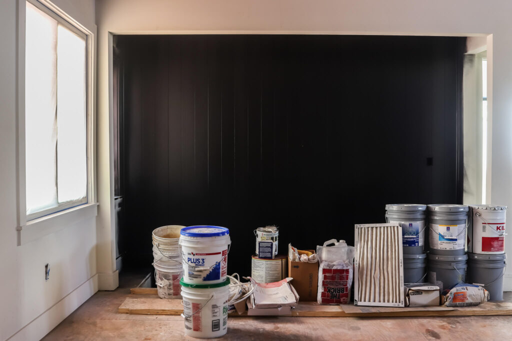 black shiplap accent wall with paint supplies sitting on floor in front of it