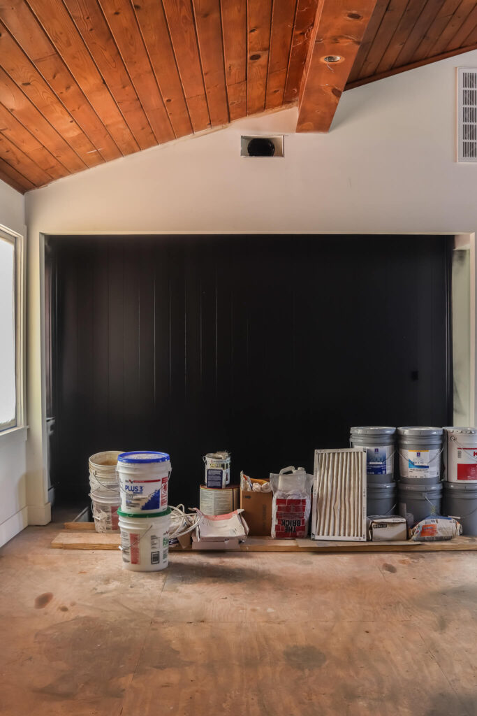 black shiplap accent wall with paint supplies sitting on floor in front of it