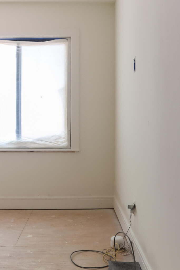 unfinished room with white walls and trim and window covered in paintes plastic