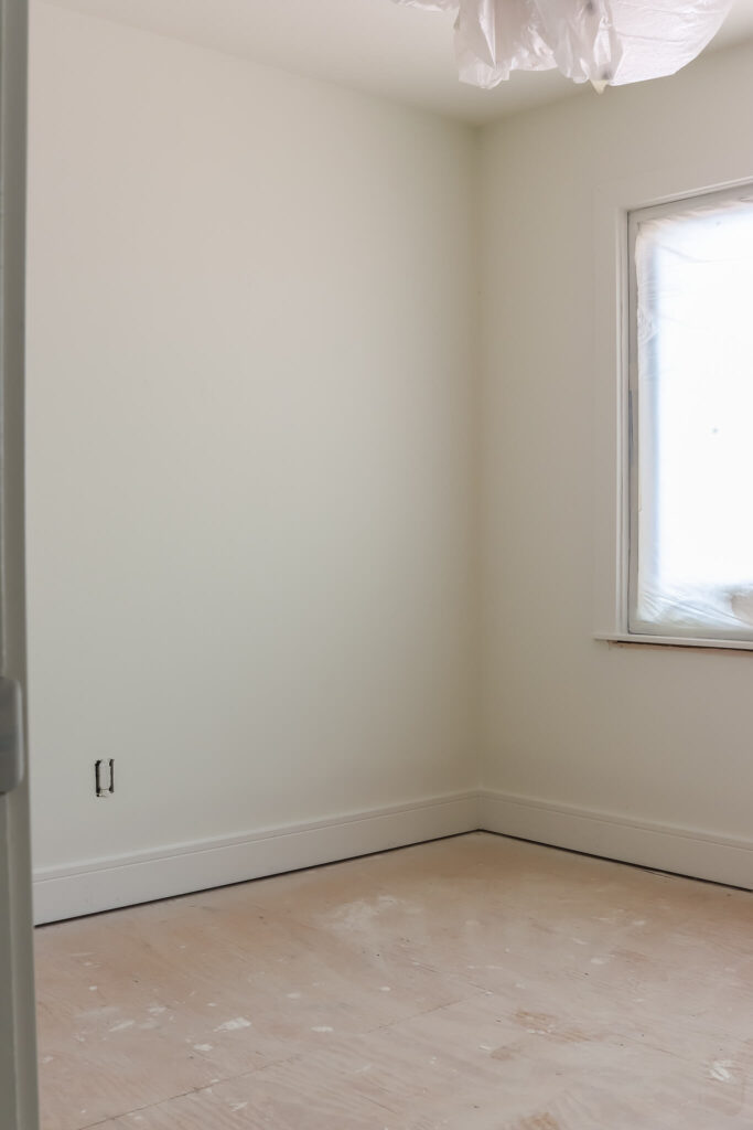 unfinished room with white walls and trim and window covered in paintes plastic
