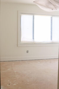 unfinished room with white walls and trim and window covered in paintes plastic