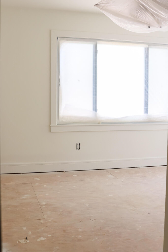 unfinished room with white walls and trim and window covered in paintes plastic