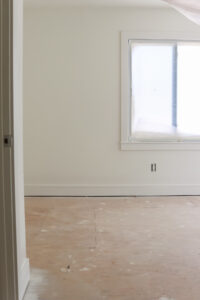 unfinished room with white walls and trim and window covered in paintes plastic