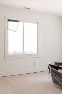 unfinished room with white walls and trim and window covered in painters plastic