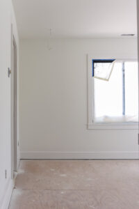 unfinished room with white walls and trim and window covered in painters plastic