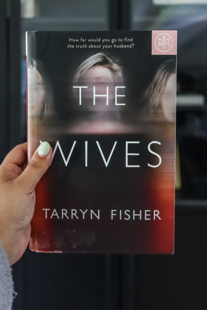woman's hand holding the wives by tarryn fisher review