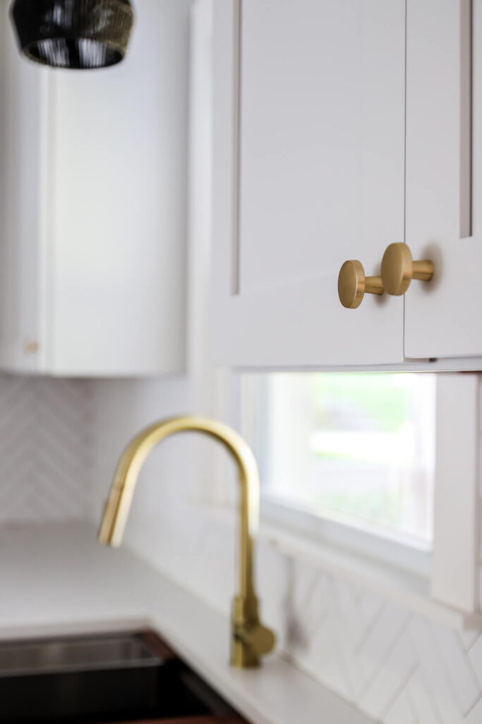 closeup of gold round knobs with gold kitchen faucet in the background