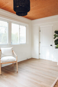 white walls in sunroom with wood ceiling and black rattan pendant