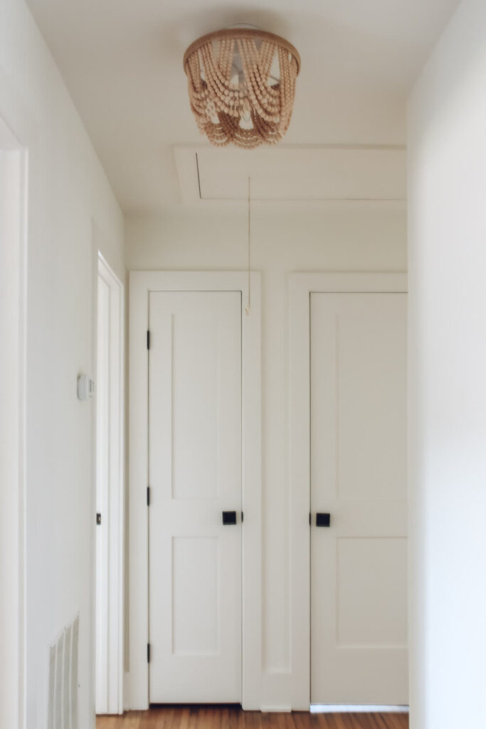 hallway with beaded flush mount light on ceiling and 2 doors with black door handles