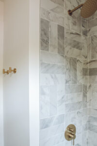 grey and white marble look subway tile in shower with gold shower faucet