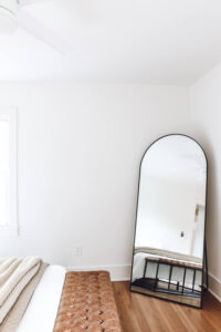 large black arched mirror in corner of bedroom with white walls