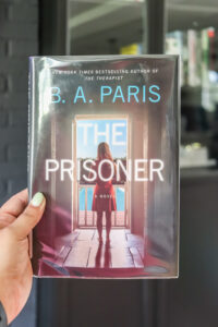 woman's hand holding BA paris the prisoner book