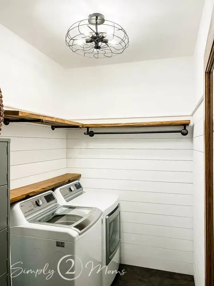 industrial pipes holding up wood shelves on shiplap wall in laundry room