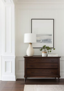 brown antique dresser with lamp and plant on it with serene painting behind it on the wall